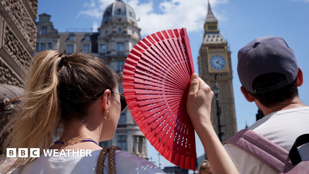 A woman on a crowded pavement near Big Ben cools herself with a bright red handheld fan