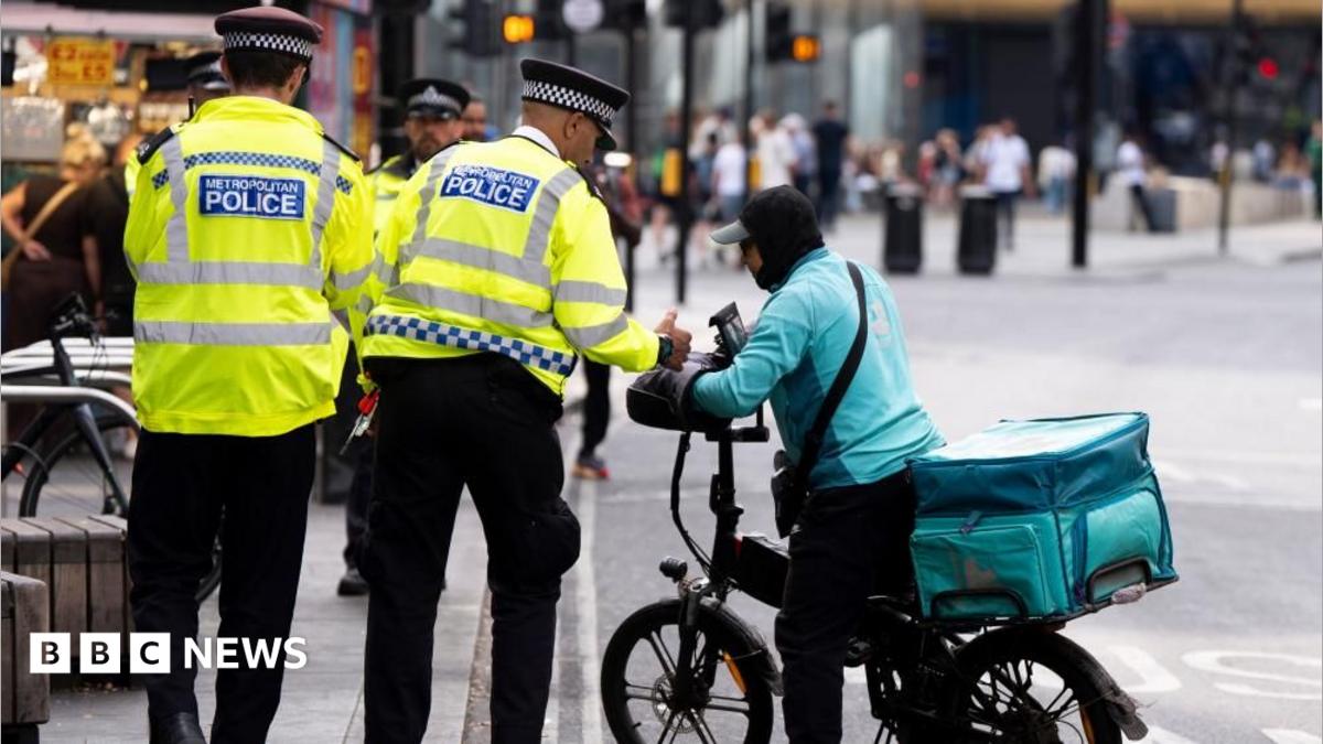 Two police officers in hi-vis can be seen at the junction of Tottenham Court Road and Oxford Street. One is seen speaking to