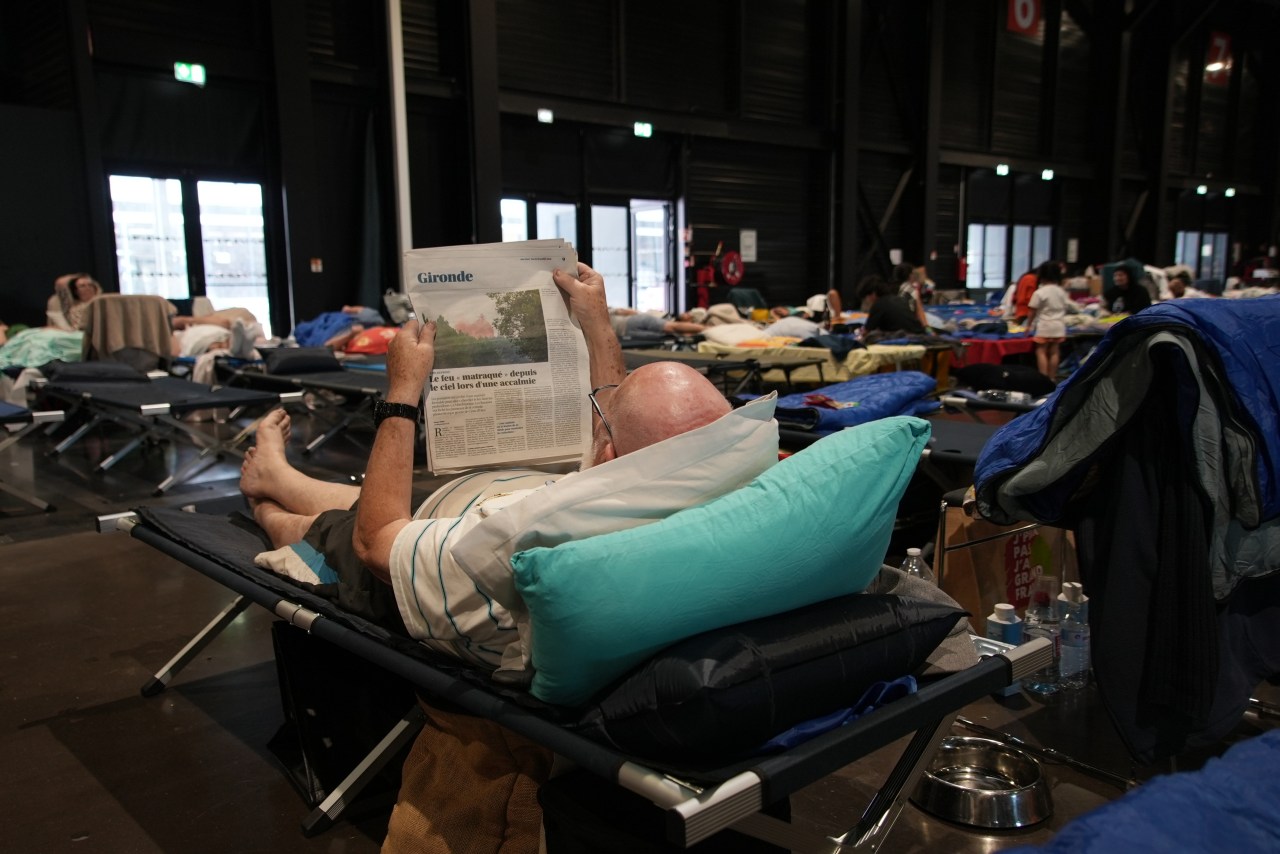 An evacuee reads a newspaper report about wildfires in southwest France as he lays on a camp bed at a temporary shelter in