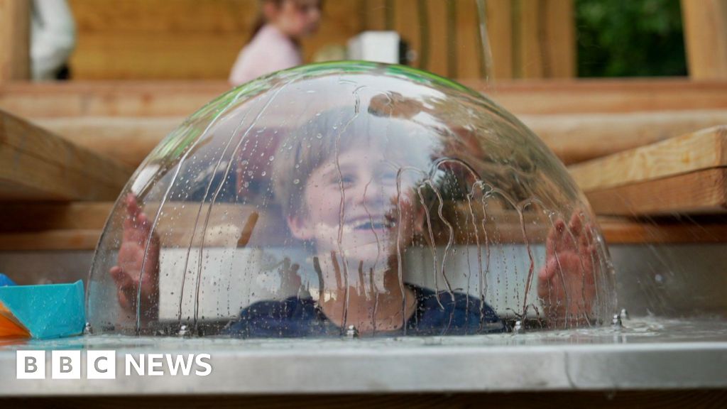 A boy pokes his head up in a glass lid, which has water dripping down the outside