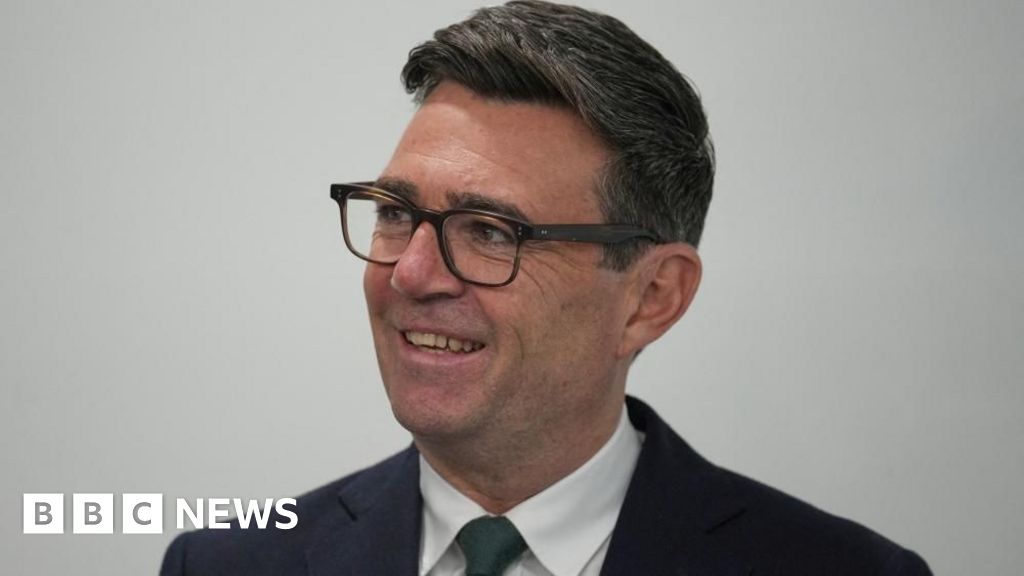 Andy Burnham looks off camera to the left. He is wearing a dark suit, white shirt and dark tie