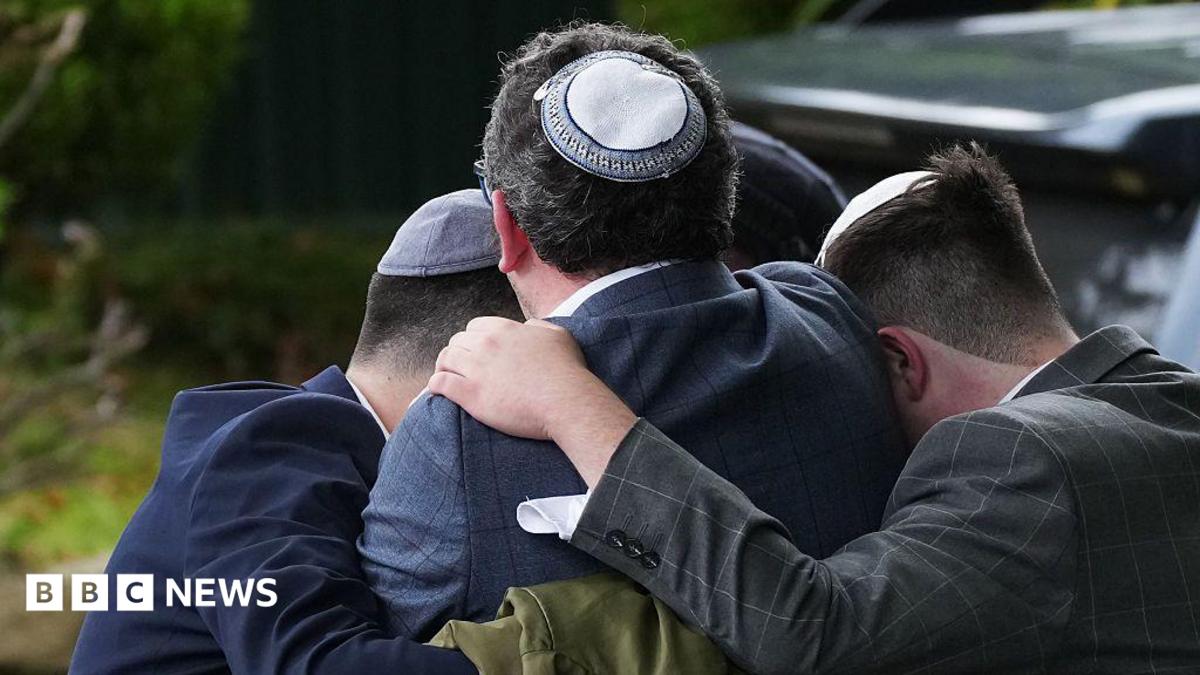 Three men wearing Jewish skullcaps - known as a kippahs - embrace in grief on the street after the attack