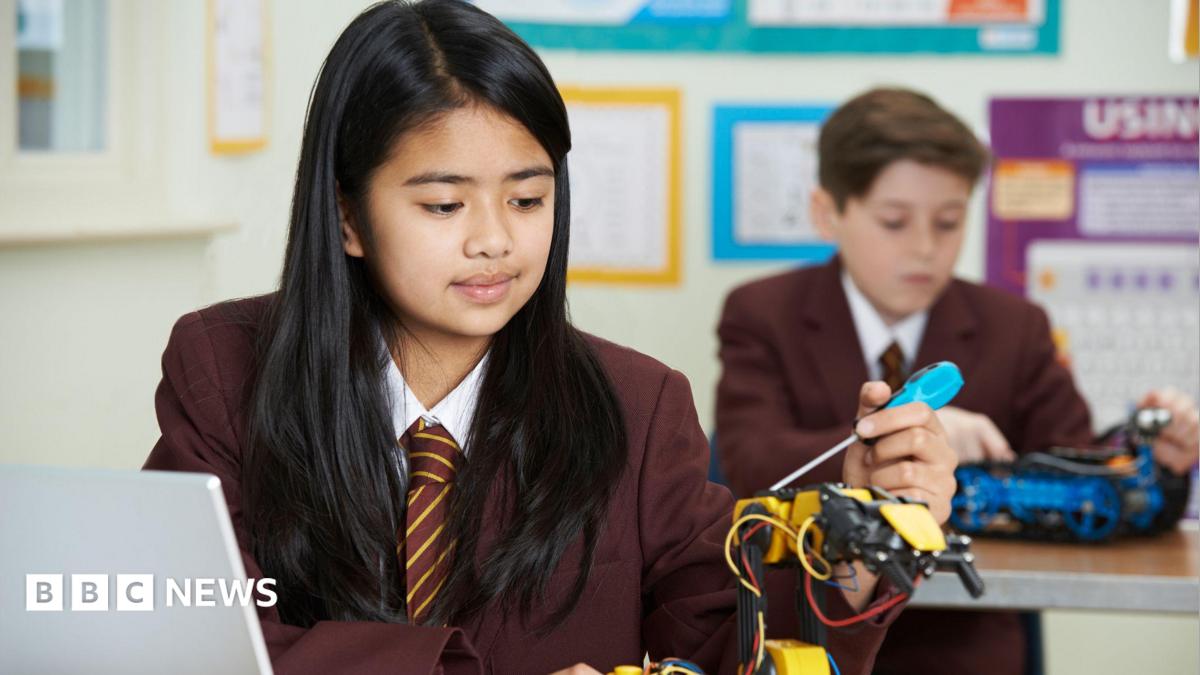 A pupil in uniform uses a tool to build a robot