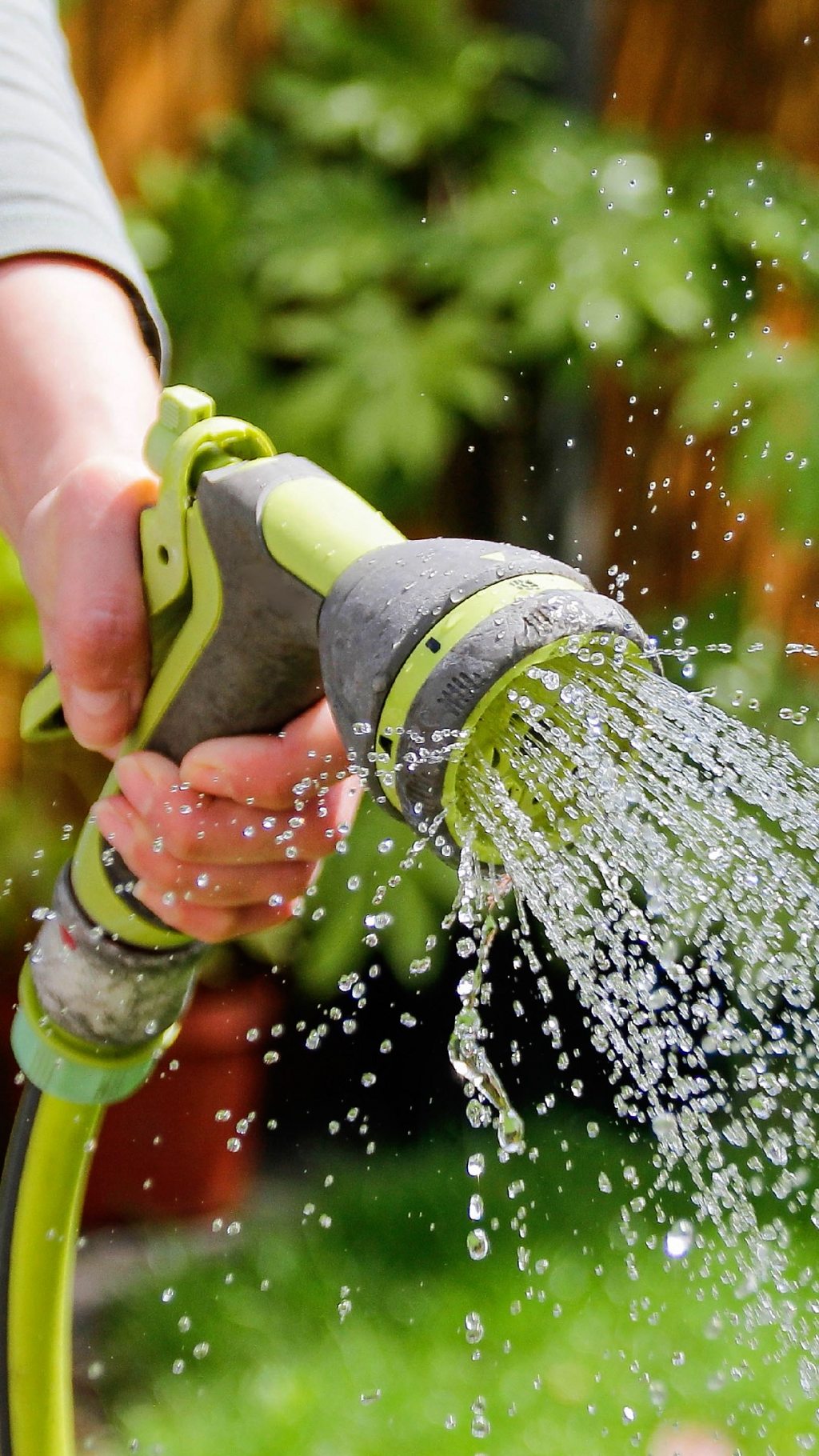 A hand holding a hosepipe spraying water