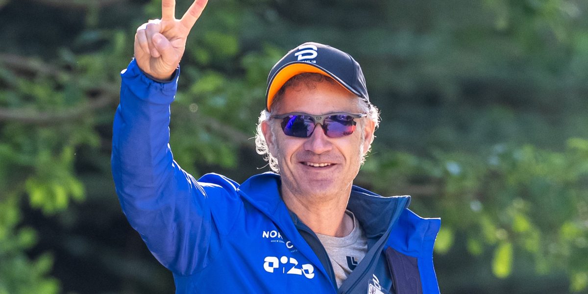 Alex Karp, wearing a hat, gives a peace sign